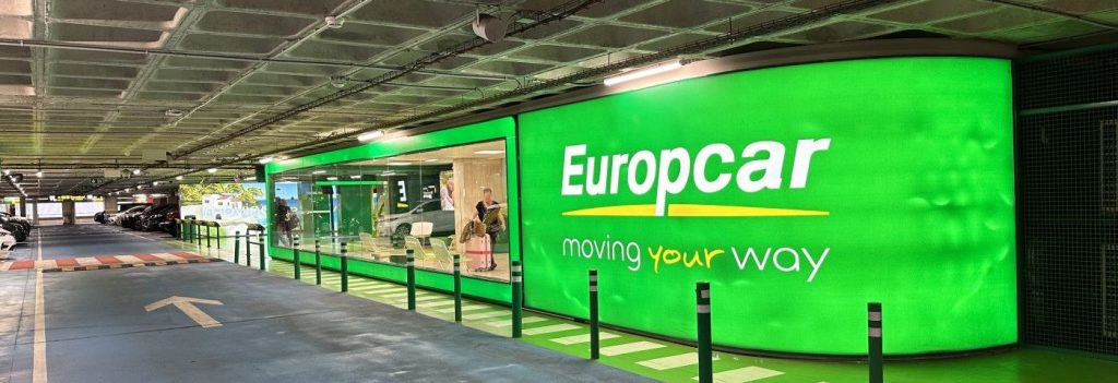 Eingangsbereich einer Europcar-Station mit grüner Leuchtreklame in einem Parkhaus