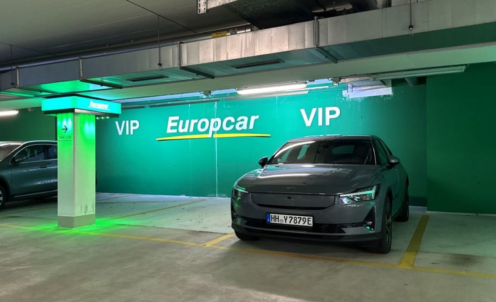 Ein Polestar 2 steht auf einem VIP-Parkplatz in einer Europcar-Tiefgarage, umgeben von grünem Licht und Branding