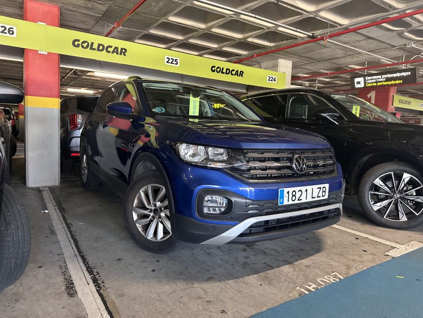 Ein blauer VW T-Cross mit dem Kennzeichen 1821 LZB steht in einem Goldcar-Parkbereich eines überdachten Parkhauses. Über dem Stellplatz sind gelbe Markierungen mit Stellplatznummern sichtbar.