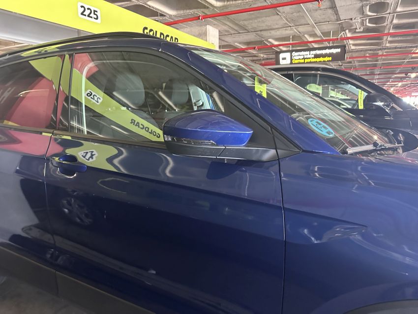 Ein blauer Mietwagen der Firma Goldcar steht auf einem gekennzeichneten Parkplatz im Parkhaus eines Flughafens auf Mallorca. Im Hintergrund sind weitere Fahrzeuge und farbige Parkschilder zu sehen.