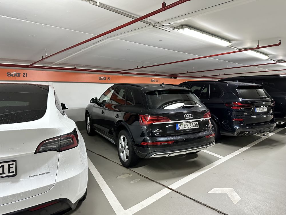 Audi Q5 auf einem reservierten Sixt-Stellplatz in einem Parkhaus, zwischen einem Tesla und einem weiteren BMW