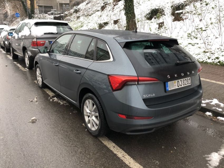 Ein grauer Škoda Scala ist auf einer nassen Straße geparkt, im Hintergrund liegen Schnee und weitere parkende Autos.